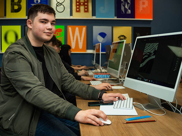 A graphic design student sat at an Apple Mac computer