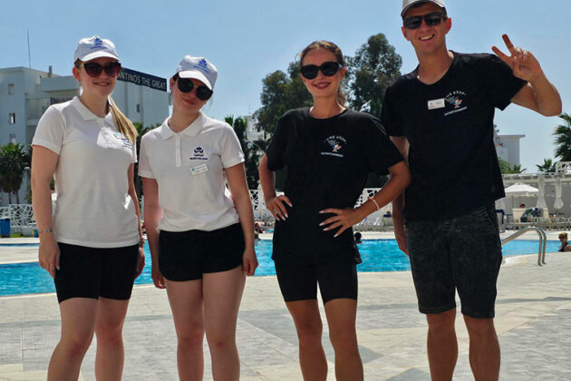 Four students stood by a swimming pool smiling at the camera