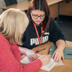 A student sat at a desk talking to a tutor