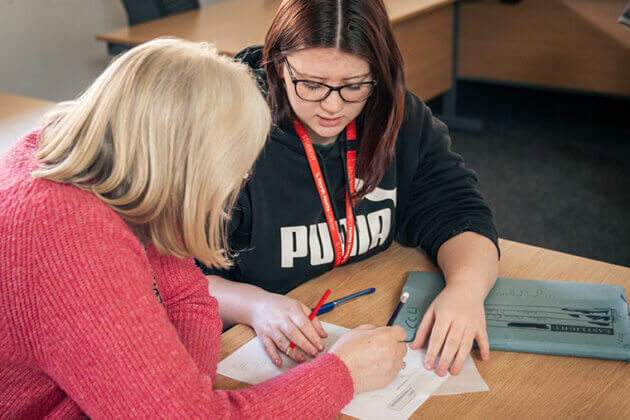 A student sat at a desk talking to a tutor