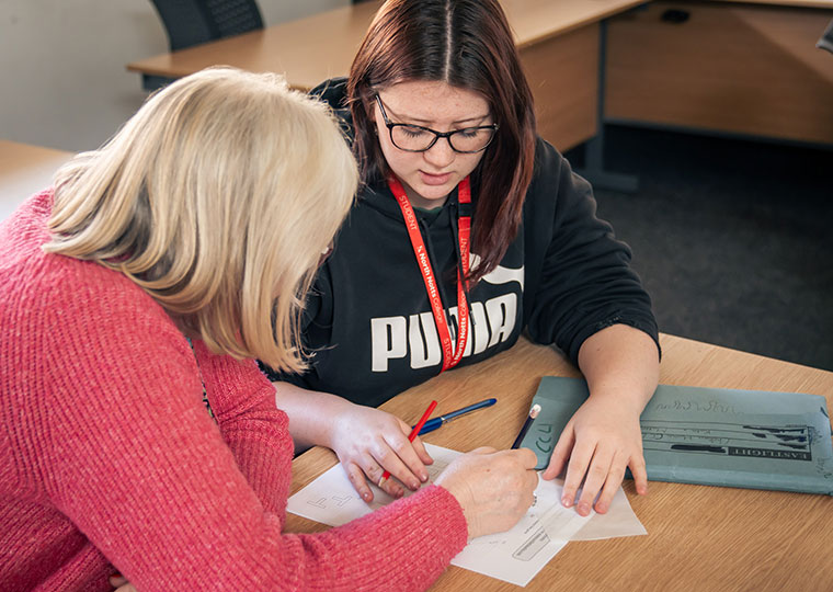 A student sat at a desk talking to a tutor