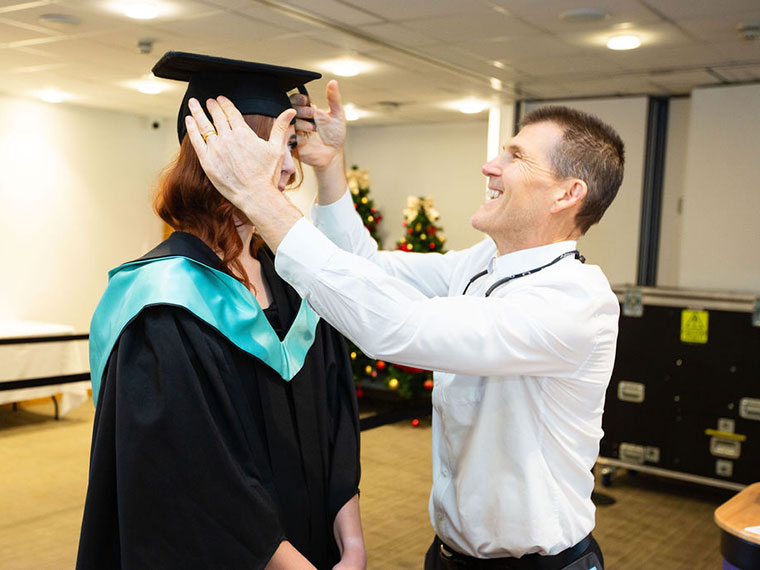 Someone adjusting a students hat at graduation 2024